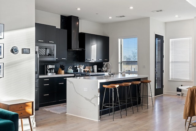 kitchen featuring wall chimney exhaust hood, stainless steel microwave, visible vents, and dark cabinets