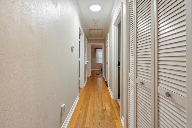 hall featuring a textured wall, attic access, light wood-style floors, ornamental molding, and baseboards