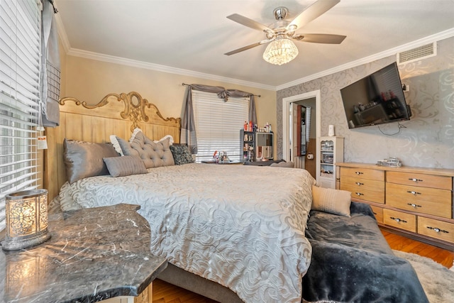 bedroom featuring ornamental molding, wood finished floors, visible vents, and wallpapered walls