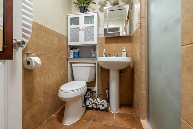 full bathroom with tile walls, toilet, a stall shower, a sink, and tile patterned floors