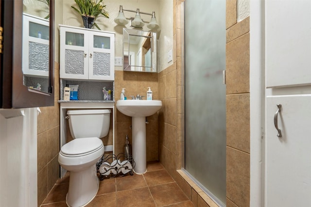 bathroom featuring tile walls, toilet, a sink, a shower stall, and tile patterned flooring