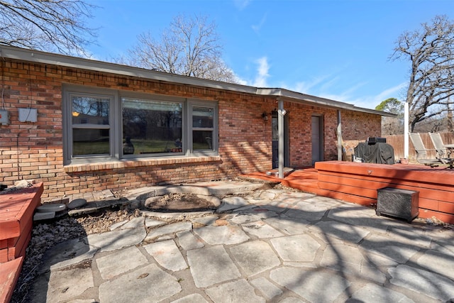 back of house featuring a patio, brick siding, a wooden deck, and fence