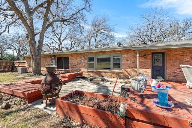 rear view of property featuring brick siding, fence, a deck, and central air condition unit