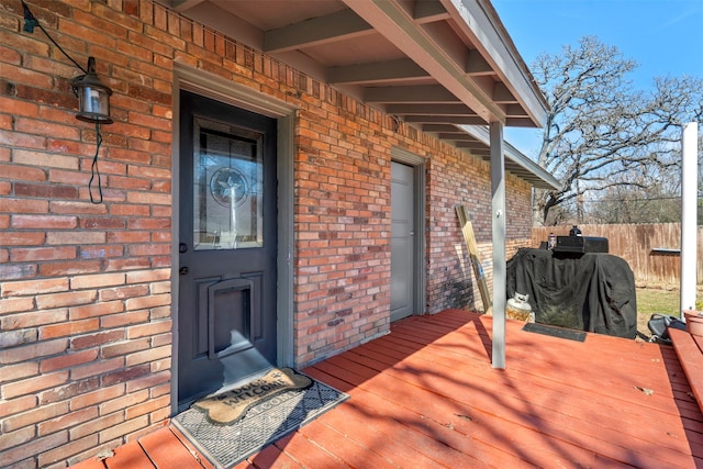 view of exterior entry with brick siding, fence, and a wooden deck