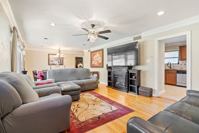 living area featuring visible vents, a glass covered fireplace, light wood-style flooring, ornamental molding, and recessed lighting