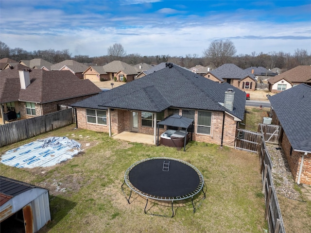 back of property featuring a fenced backyard, a trampoline, a residential view, and brick siding