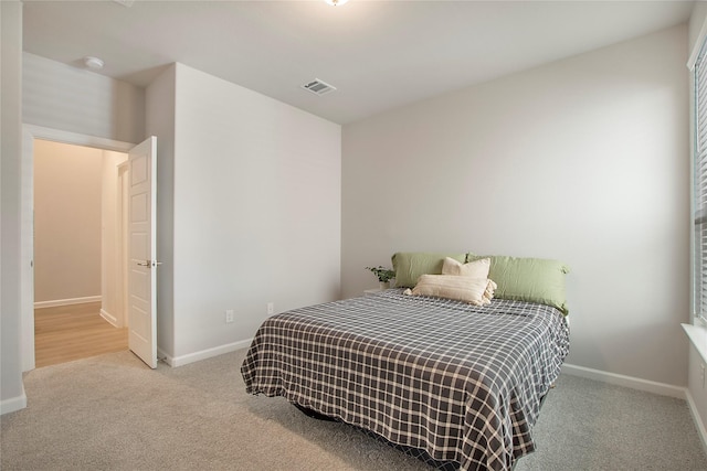 bedroom with baseboards, visible vents, and light colored carpet