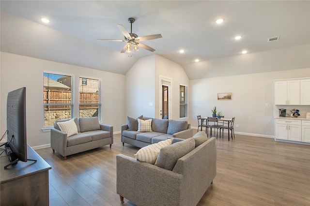 living room featuring light wood finished floors, baseboards, visible vents, and vaulted ceiling