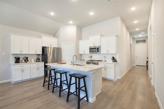 kitchen featuring a center island with sink, white cabinets, appliances with stainless steel finishes, a breakfast bar, and light countertops