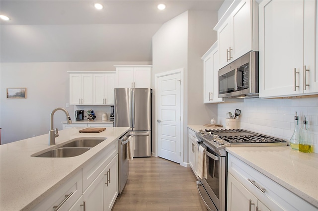 kitchen with stainless steel appliances, a sink, light wood-style floors, white cabinets, and light stone countertops