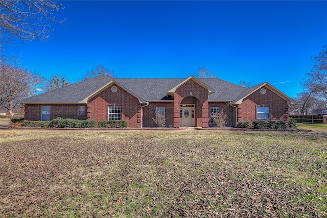 ranch-style house featuring roof with shingles, brick siding, and a front lawn