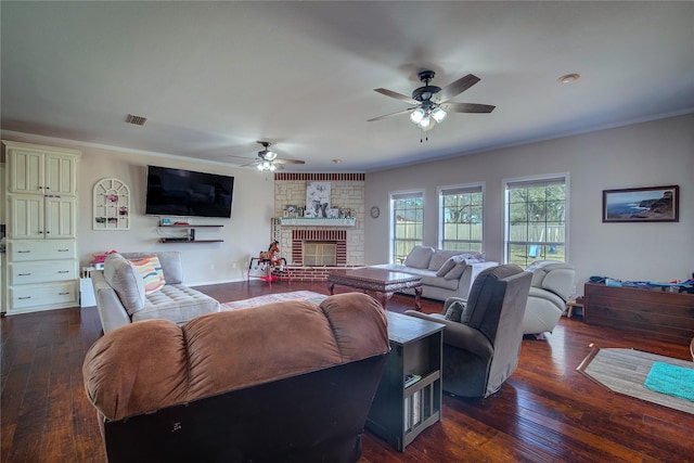 living room with crown molding, visible vents, dark wood-type flooring, a brick fireplace, and ceiling fan