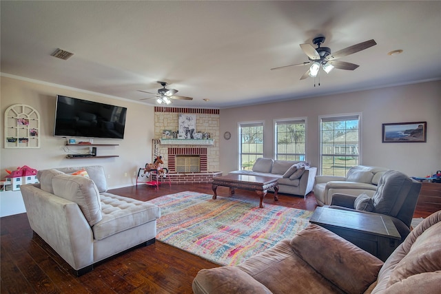 living area featuring visible vents, dark wood finished floors, ceiling fan, ornamental molding, and a brick fireplace