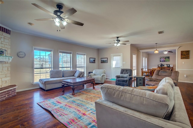 living area featuring baseboards, visible vents, dark wood-type flooring, crown molding, and a fireplace