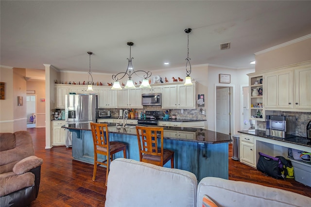 kitchen featuring appliances with stainless steel finishes, dark countertops, a center island with sink, and pendant lighting