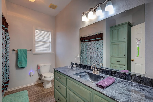 bathroom with toilet, wood finished floors, vanity, visible vents, and baseboards