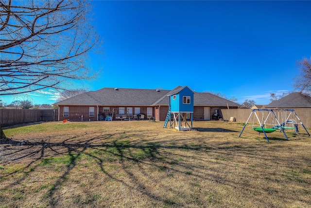 rear view of property featuring a playground, a yard, and a fenced backyard