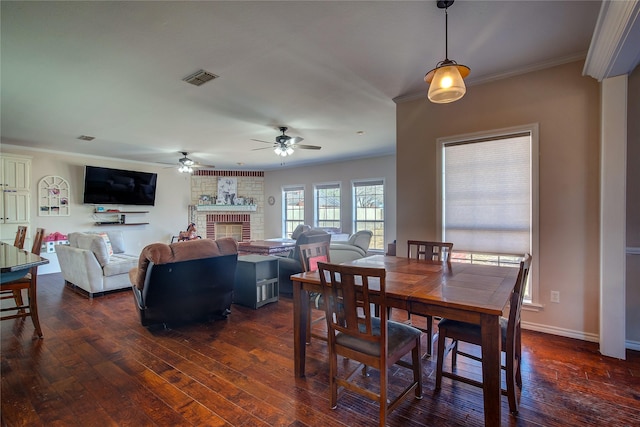 dining area featuring baseboards, visible vents, ornamental molding, dark wood-style flooring, and a brick fireplace