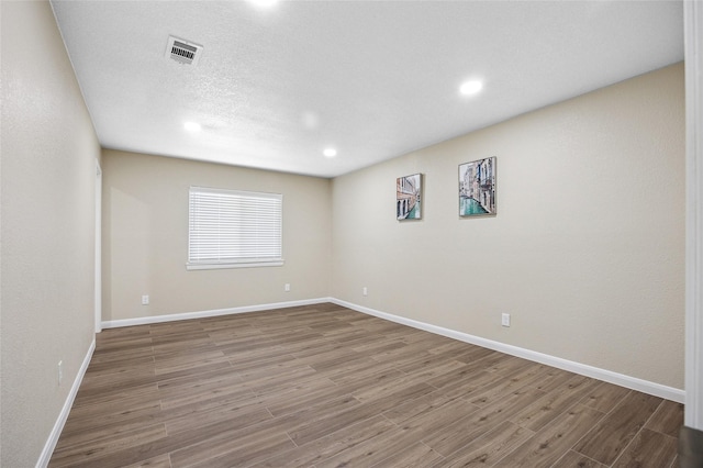 empty room with a textured ceiling, recessed lighting, wood finished floors, visible vents, and baseboards