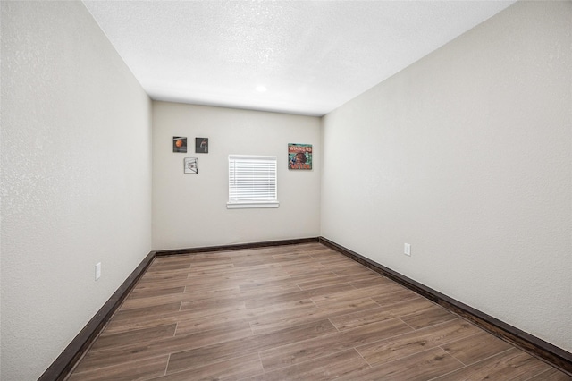 empty room featuring a textured wall, a textured ceiling, baseboards, and wood finished floors