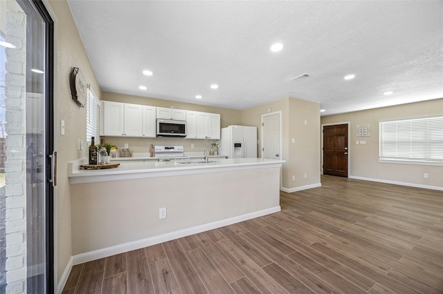 kitchen with a sink, wood finished floors, white appliances, a peninsula, and baseboards