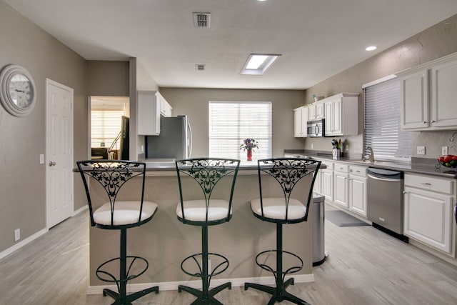 kitchen featuring dark countertops, visible vents, appliances with stainless steel finishes, white cabinets, and a kitchen bar