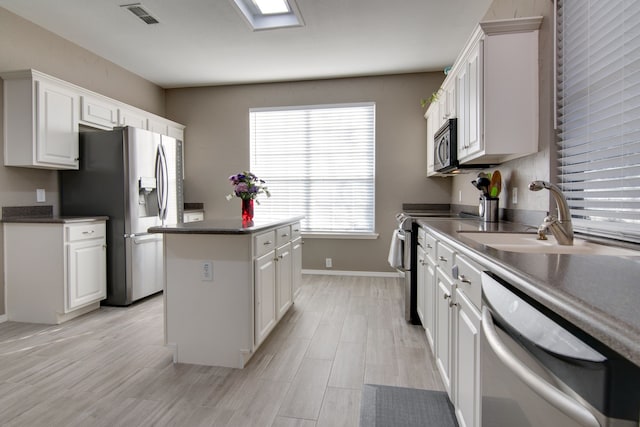 kitchen featuring a center island, visible vents, appliances with stainless steel finishes, white cabinetry, and a sink