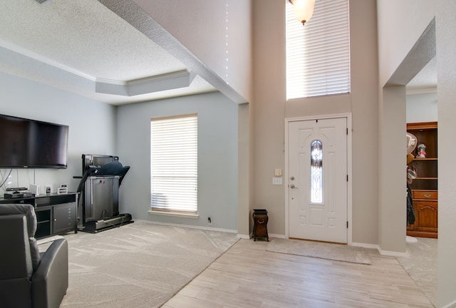 entryway with a raised ceiling, a healthy amount of sunlight, crown molding, and a textured ceiling