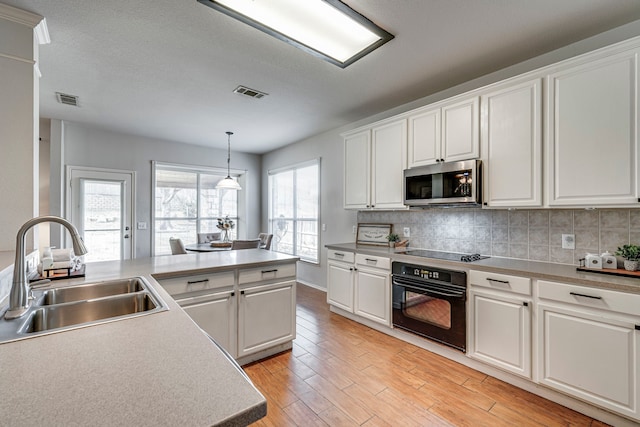 kitchen featuring visible vents, light wood-style flooring, a sink, black appliances, and backsplash