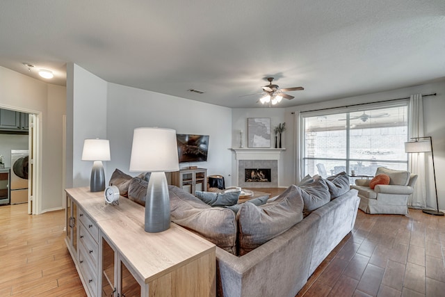 living room featuring a tile fireplace, washer / clothes dryer, visible vents, and wood finished floors