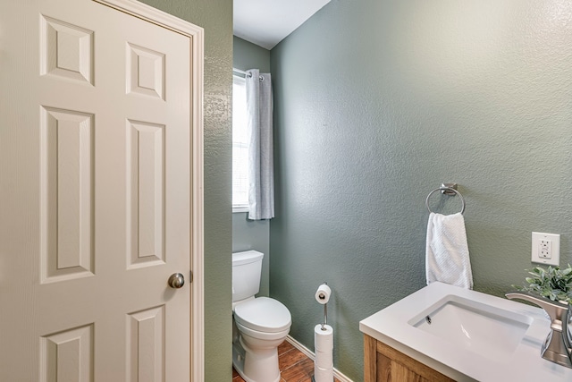 half bath featuring toilet, a textured wall, a sink, and wood finished floors