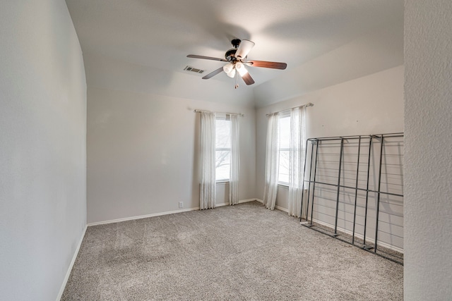 carpeted spare room with lofted ceiling, baseboards, visible vents, and ceiling fan