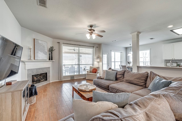 living area with decorative columns, visible vents, ceiling fan, light wood-type flooring, and a fireplace