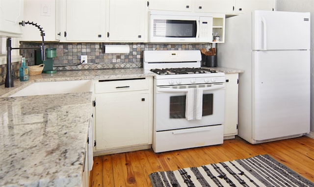 kitchen featuring white appliances, light wood-style flooring, light stone countertops, white cabinetry, and backsplash