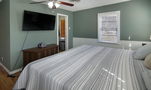 bedroom with wainscoting, wood finished floors, and a ceiling fan