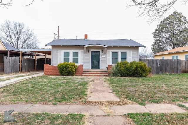 bungalow with an attached carport, brick siding, fence, and a front yard