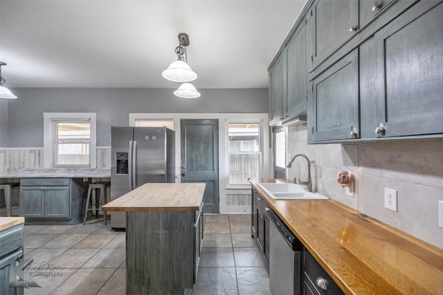 kitchen featuring wood counters, a center island, hanging light fixtures, stainless steel appliances, and a sink