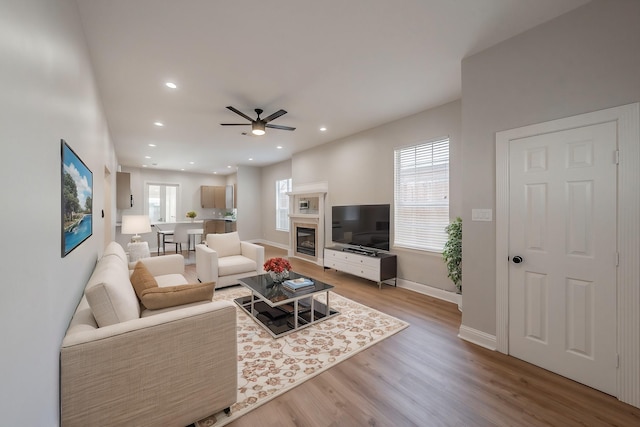 living area featuring recessed lighting, wood finished floors, a ceiling fan, baseboards, and a glass covered fireplace