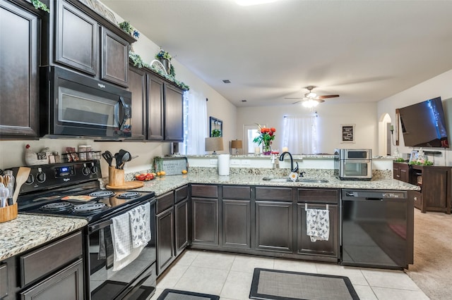 kitchen with light stone counters, a peninsula, dark brown cabinets, black appliances, and a sink