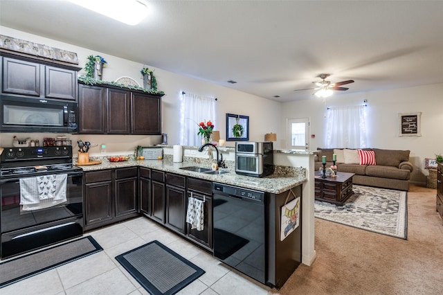 kitchen featuring open floor plan, a peninsula, light stone countertops, black appliances, and a sink