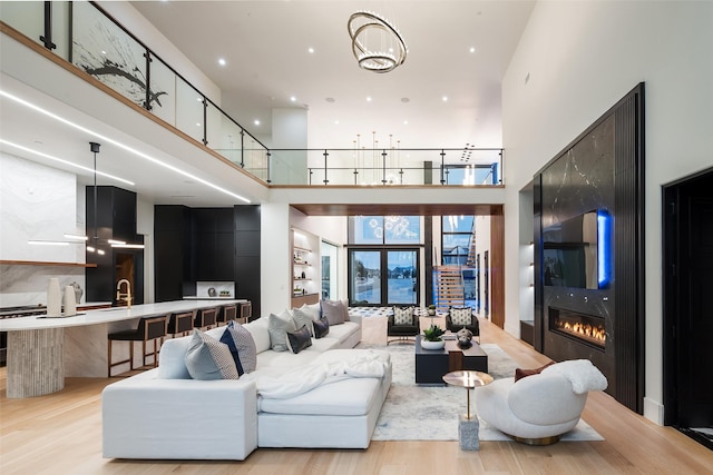 living area featuring a towering ceiling, a glass covered fireplace, and light wood-style flooring