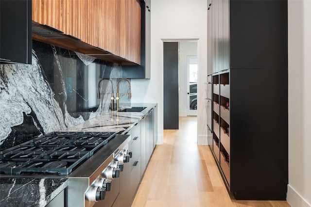 kitchen featuring light wood finished floors, decorative backsplash, stove, dark stone countertops, and a sink