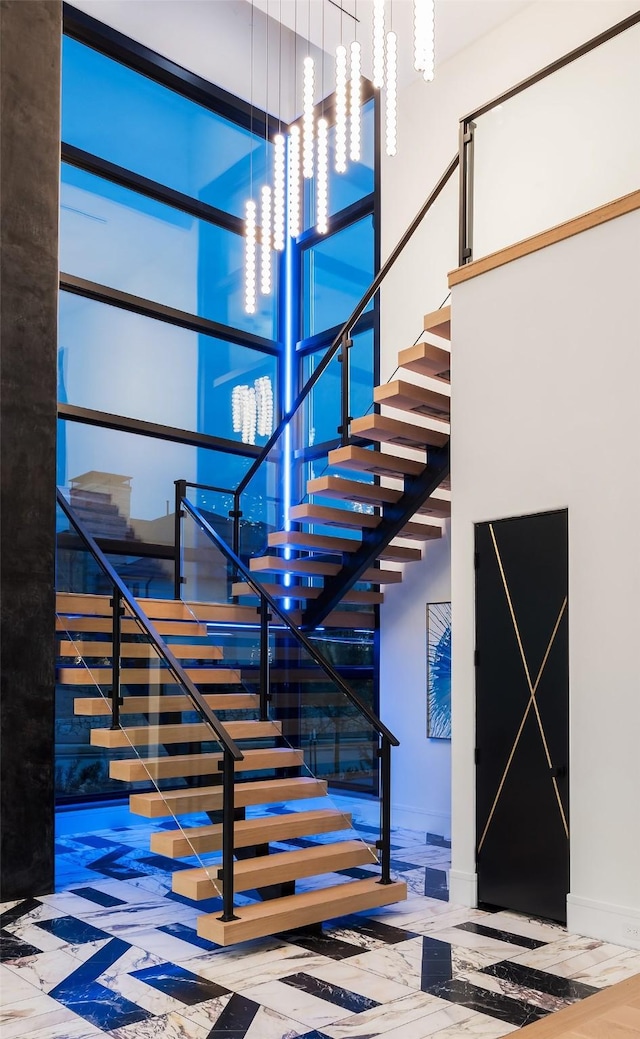 stairway with a towering ceiling, an inviting chandelier, and baseboards