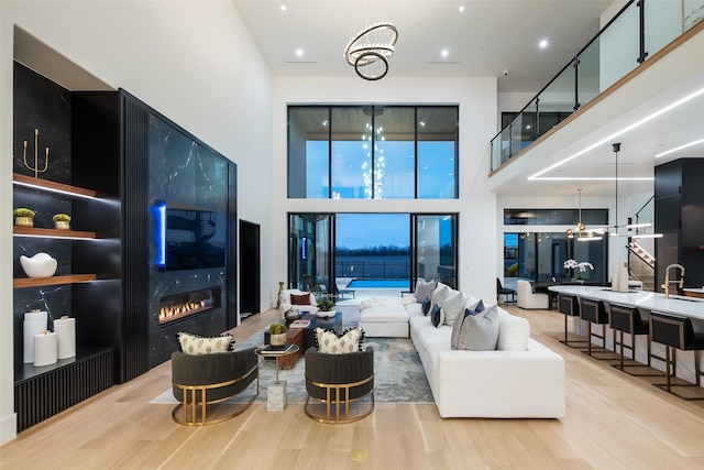 living area featuring light wood finished floors, a premium fireplace, a high ceiling, and a notable chandelier