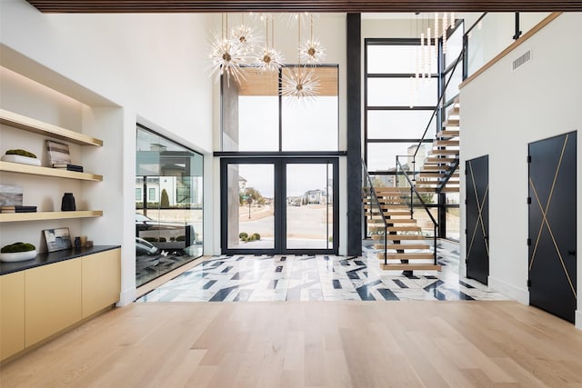 entryway featuring visible vents, a towering ceiling, an inviting chandelier, stairs, and floor to ceiling windows