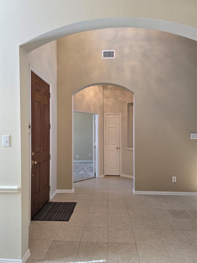 tiled foyer entrance with baseboards, visible vents, and arched walkways