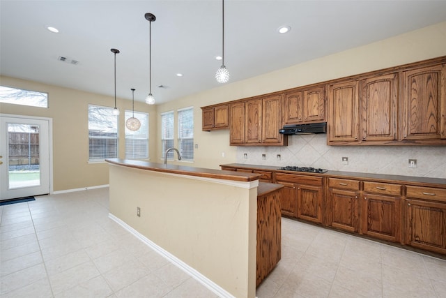 kitchen with black stovetop, tasteful backsplash, visible vents, brown cabinetry, and under cabinet range hood