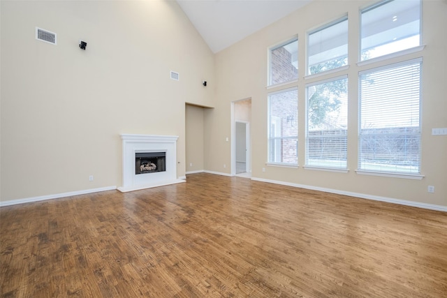 unfurnished living room with baseboards, visible vents, a fireplace with raised hearth, and wood finished floors