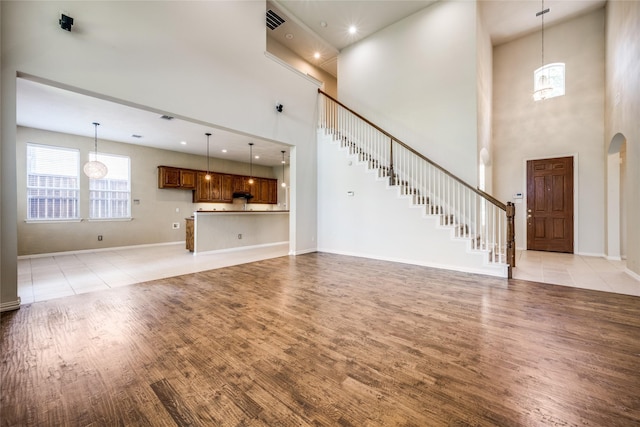 unfurnished living room featuring light wood-style floors, baseboards, stairs, and visible vents