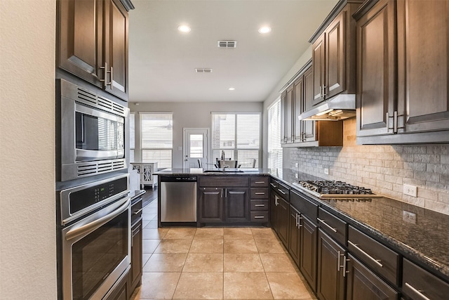 kitchen with tasteful backsplash, visible vents, dark stone counters, stainless steel appliances, and under cabinet range hood